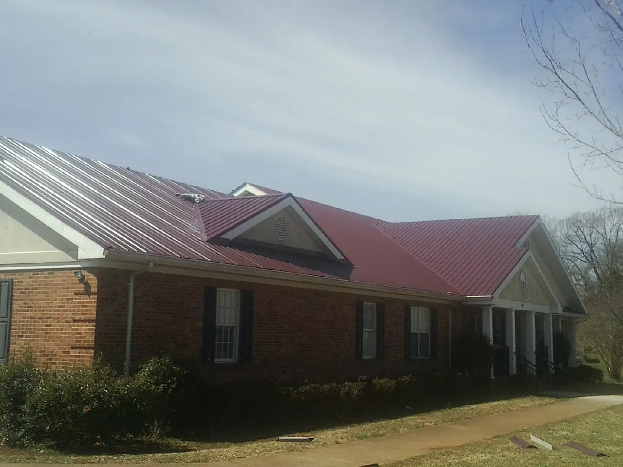 Red metal roof with gabled entries on a long brick building, from a Hail Damage Roof Repair job in Bombay