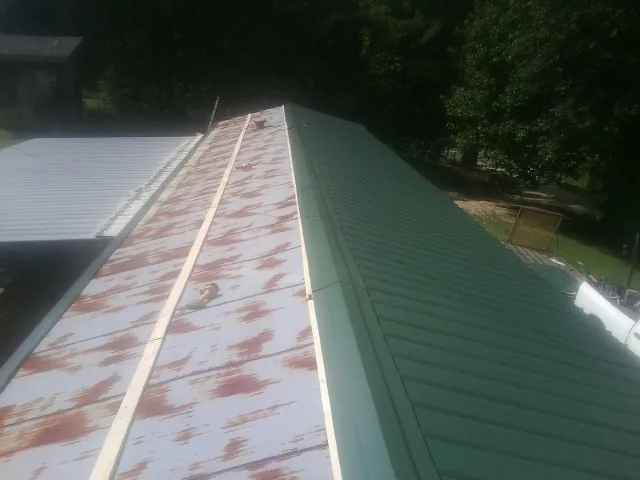 Old rusted panels beside newly installed green metal roofing — Wind Damage Roof Repair by Roofing Brothers in Bombay