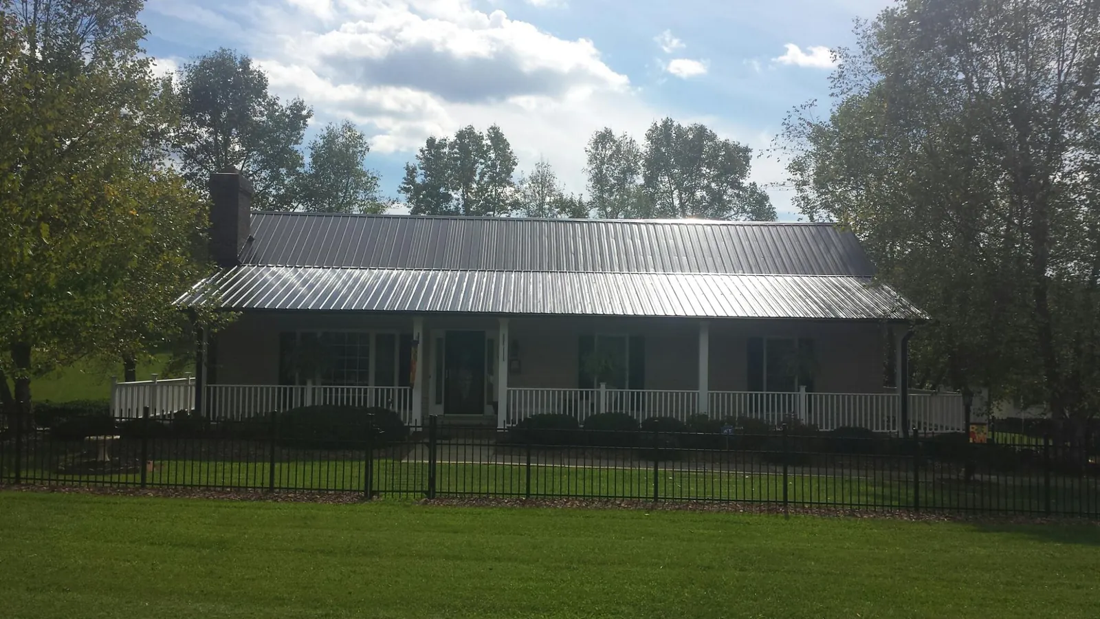 Gray metal roof on a brick ranch with a full width front porch — Gutter Guard Installation work by our crew in Bombay